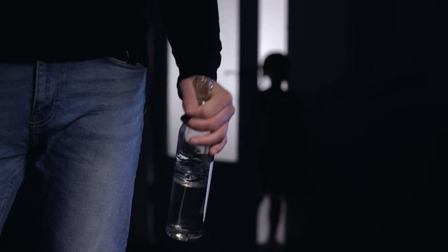 Father with alcohol bottle watching scared daughter silhouette running away
