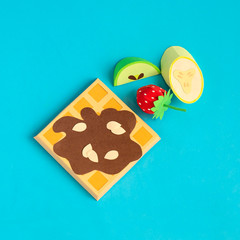 Belgian waffles with chocolate syrup and pieces of fruit made of paper