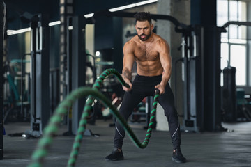 Obraz na płótnie Canvas Fitness man working out with battle ropes at gym