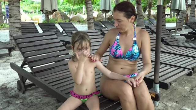 Mom applies sunscreen to baby's skin. Woman in bikini and her daughter on the beach.