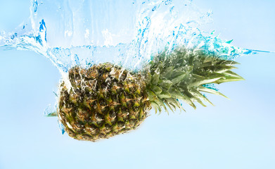 Fresh ripe pineapple falling in water with splash