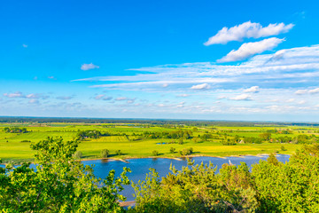 Naklejka premium View over the Elbauen in Lower Saxony, Germany. You see a landscape with fields, meadows and the river Elbe under a blue sky with white clouds.