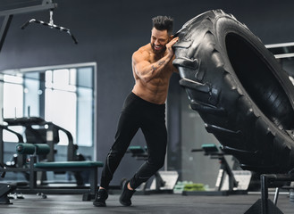 Naked man flipping huge tire at gym