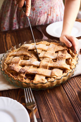 Woman putting delicious american pie on table. Close-up woman's hands cutting a homemade apple pie. White plates on the table