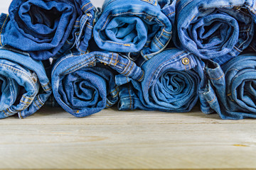 top view of roll blue denim jeans arranged in stack on wooden shelf. Beauty and fashion clothing concept
