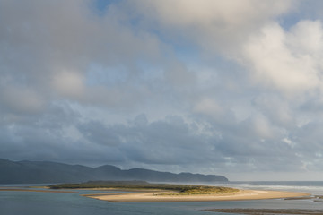 The golden light of sunset spotlights a sandy beach on an island under a cloudscape of dramatic clouds - Netarts, Oregon
