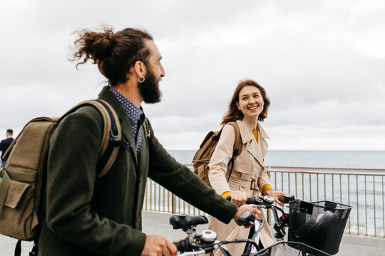 Smiling couple with e bikes walking on promenade