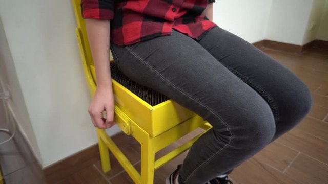 close-up of a girl in a red-black klechaty shirt and jeans sitting on a bright yellow chair studded with sharp nails