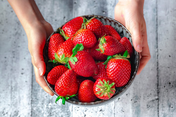 Bowl with fresh strawberries, hands of a girl