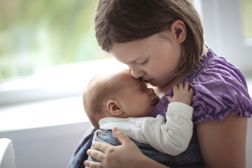 older sister hugs baby in sling, newborn baby