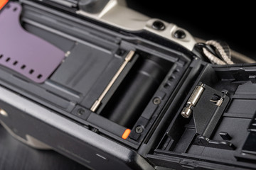 Old analog camera and black and white new film. Accessories for analog photography on a dark table.