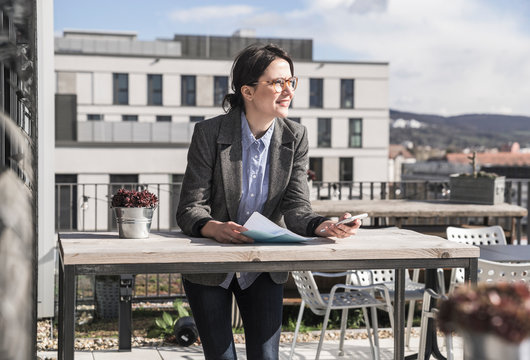 Smiling businesswoman using cell phone on roof terrace