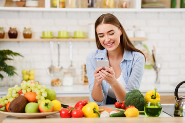 Young Woman Texting when Cooking In Kitchen