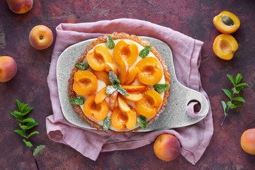 Top view of apricot tart with mint leaf on ceramic board on dark background