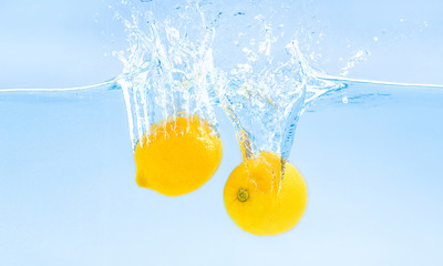 Fresh lemons sinking into water with splash