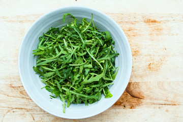 healthy fresh green peppery rocket leaves in a bowl on a wooden chopping board