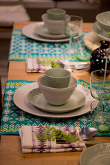 Festive table setting in white and green tones. Plates wine glasses on ethnic napkin with ornament