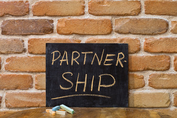Fototapeta premium Chalk board with the word PARTNERSHIP drown by hand and chalks on wooden table on brick wall background.