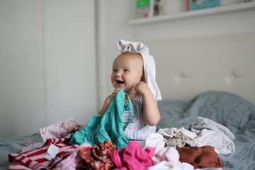 Funny Caucasian baby playing with bunch of clothes