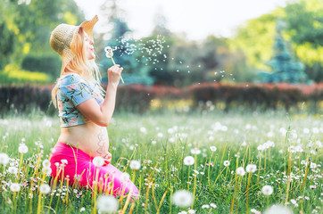 pregnant woman with mehendi pattern on belly blows on dandelion