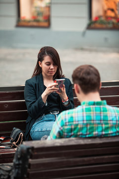 communication problem man with woman sitting on bench at city street drinking coffee in paper cup looking ito phones