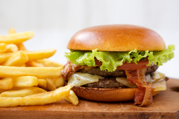 Hamburger and french fries on a rustic wooden board, side view. Close-up.