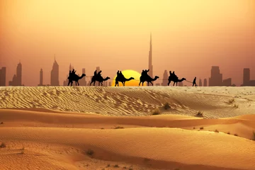 Foto auf Acrylglas Dubai-Skyline am Horizont mit Kamelritt-Wohnwagen-Silhouette in der Wüste © adrian_ilie825