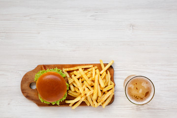 Hamburger, french fries, sauce and glass of cold beer on a white wooden surface, top view. Overhead, flat lay, from above. Copy space.