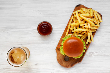 Hamburger, french fries, sauce and glass of cold beer on a white wooden background, top view. Overhead, flat lay, from above.
