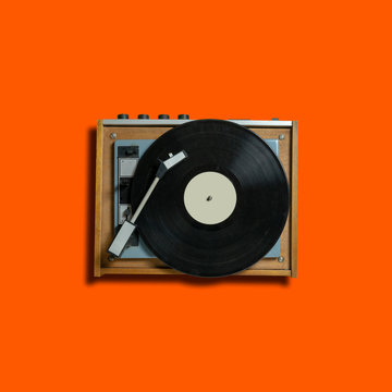 vintage turntable vinyl record player on orange background. retro sound technology to play music