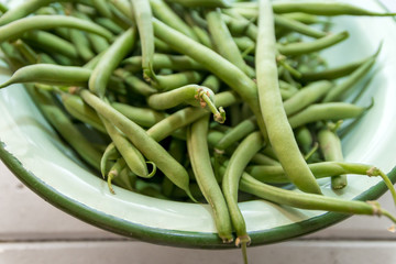 Freshly picked organic grean beans in a vintage enamel bowl on a white whashed table