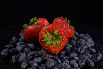 Dark honeysuckle berries and sweet strawberries against black background, place for text. Concept...