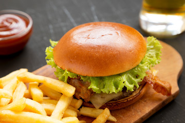 Tasty amburger, french fries, sauce and glass of cold beer on a black background, side view. Close-up.