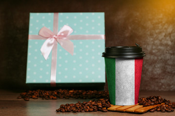 Paper cup for coffee with the image of the Italian flag. Grains lie on a wooden surface.