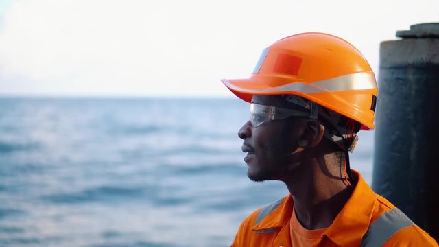 Tired Seaman AB or Bosun on deck of vessel or ship , wearing PPE personal protective equipment - helmet, coverall, lifejacket, goggles. Safety at sea