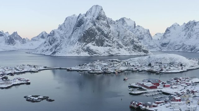Winter scene of authentic village Reine on Lofoten Islnads Archipelago in Norway. Drone video from above. Snowy mountain peaks, ocean and coastal fishing village with classic red wooden houses.