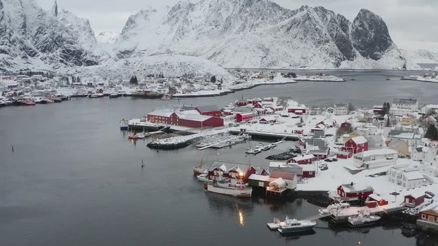 Winter scene of authentic village Reine on Lofoten Islnads Archipelago in Norway. Drone video from above. Snowy mountain peaks, ocean and coastal fishing village with classic red wooden houses.