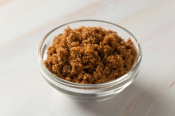 Brown sugar isolated in glass bowl, over styled marble background. Top view, copy space.