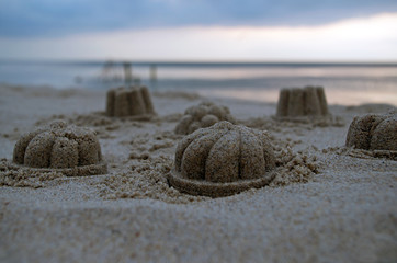 Children's figures of gray sand dome shaped with curls and bumps on blurred background sea and blue...