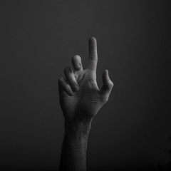 Male hand pointing a finger against a dark background. Selecting, touching