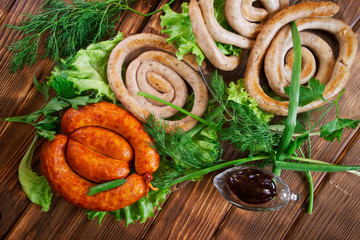Country breakfast. Grilled pork sausages and sauce on a wooden surface made of pine boards. Next to it are lettuce, parsley, dill and onion. Picnic - barbecue