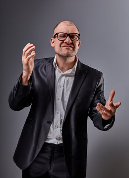 Thinking angry bald business man in eyeglasses and suit discussing and moving the hands  on grey background.