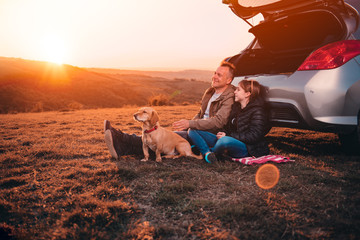 Father and daughter with dog camping on a hill by the car during sunset