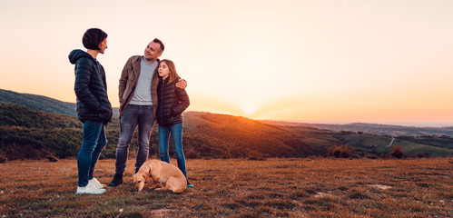 Family with dog embracing while standing on the hill