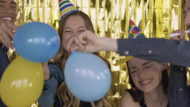4 happy cheerful people at a party in paper festive hats fight balloons. A group of laughing people of mixed race on a gold background. HD