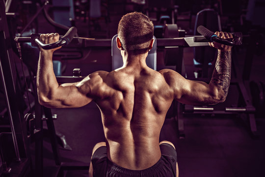 Young Muscular Man Doing Hard Exercise With Dumbbells For Average Deltas Of Shoulders In Training Machine At The Gym.