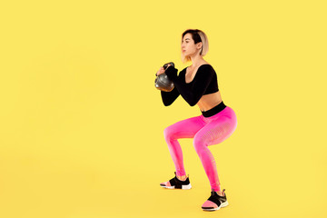 Fototapeta na wymiar Fitness woman in fashionable pink and black sportswear work out with kettlebell on yellow background. Strength and motivation.