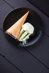 Ice cream cone on black background, summer concept. Dessert with jam on black plate. Waffle cone with ice cream in minimalism style. Copy space