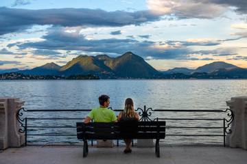 Tourist couple sits on bench and observes the romantic sights of lake at sunrise