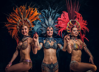 Three beautiful young womans in traditional brasilian carnaval costumes are posing for photographer...